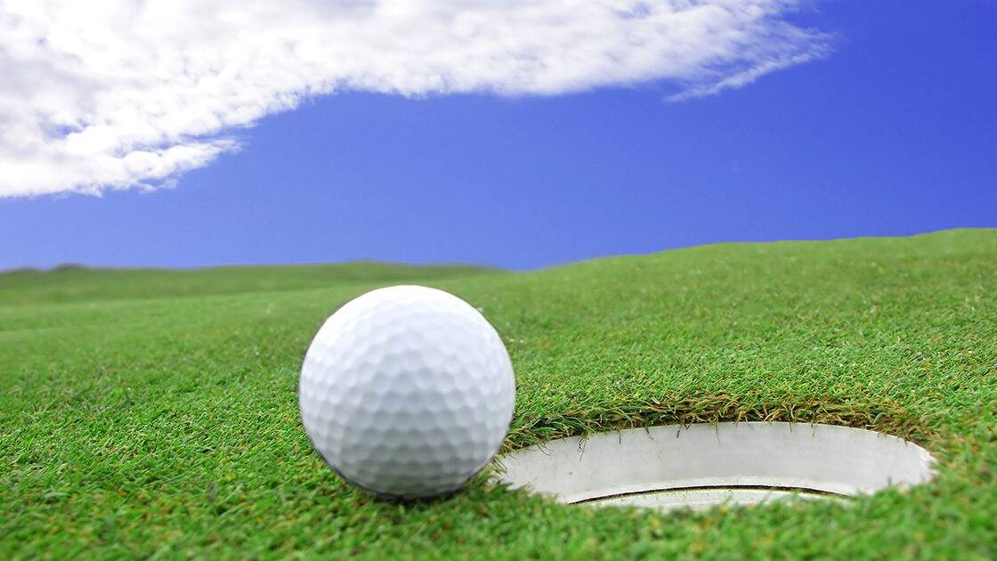 Eco-Friendly Lifestyle: Close-up of a golf ball on a golf course, embodying an eco-friendly lifestyle choice, under clear skies with light clouds.